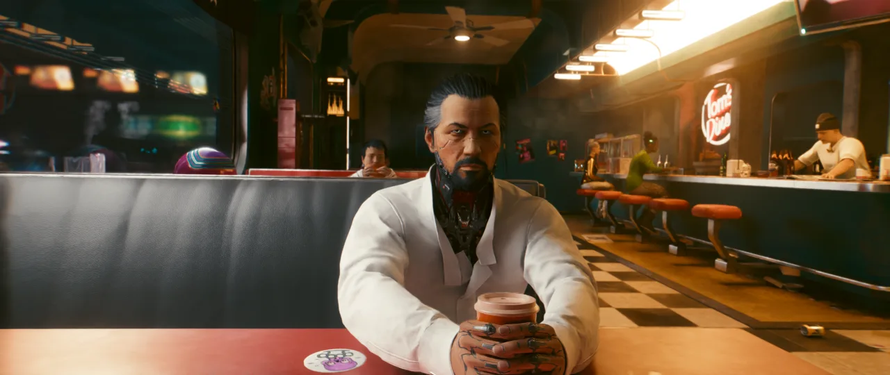 A bearded man in a white jacket sits alone at a diner-style counter, holding a cup as warm neon lighting and a checkerboard floor give the *Cyberpunk 2077* scene a moody, late-night feel.