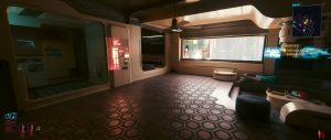 A quiet interior scene from *Cyberpunk 2077*, showing a sleek futuristic room with patterned flooring, curved walls, built-in seating, and soft neon-lit details, while the game UI remains visible on screen.