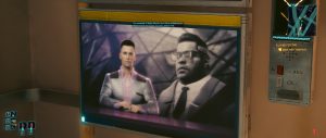 A wall-mounted screen in a sleek interior shows a broadcast-style image of two sharply dressed figures, framed by the warm, futuristic design typical of *Cyberpunk 2077*. The shot focuses on the in-world display and surrounding details, giving the scene a quiet, story-driven atmosphere.