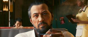 A close-up conversation scene from *Cyberpunk 2077*, centered on Takemura as he sits in a warm, upscale interior with a drink in hand, while other figures and soft lighting in the background reinforce the quiet, story-focused atmosphere.